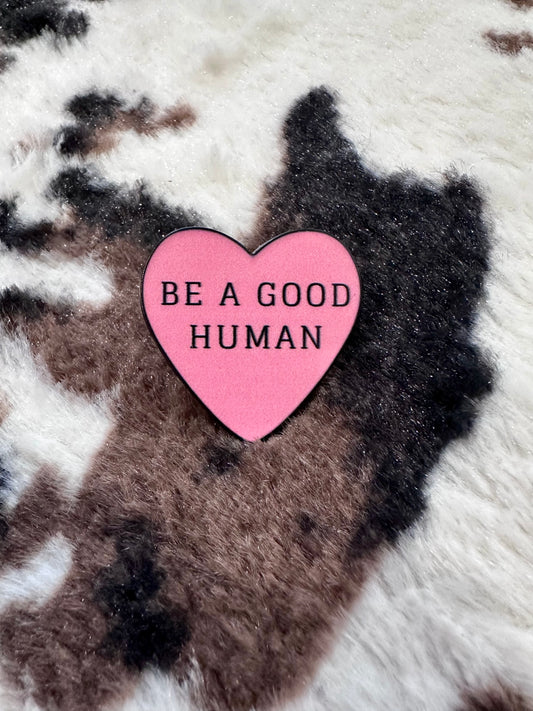 'be a good human' slogan heart shaped pink pin. 